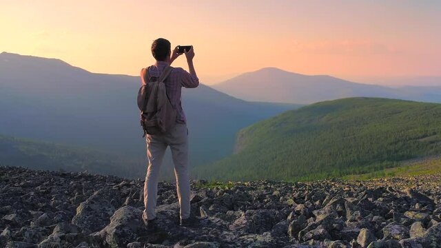 A man in the mountains photographs the landscape on his smartphone. A tourist with a backpack photographs the sunset on a mountain pass. Hiking in the mountains of the Northern Urals.