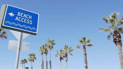 Beach sign and palms in sunny California, USA. Palm trees and seaside signpost. Oceanside pacific tourist resort aesthetic. Symbol of travel holidays and summertime vacations. Beachfront promenade