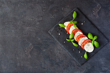 Caprese salad with mozzarela, tomatoes, fresh olive oil and basil on slate board on black background top view.