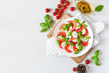 Caprese salad with mozzarela, tomatoes, fresh olive oil and basil on white background top view.