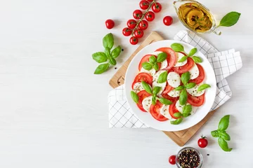 Poster Im Rahmen Caprese salad with mozzarela, tomatoes, fresh olive oil and basil on white background top view. © Inna Dodor