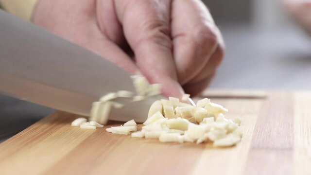 cutting garlic with a knife on a wooden board close-up. cooking lunch at home