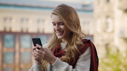 Fototapeta premium Excited girl looking phone screen outdoors. Joyful woman holding phone on street