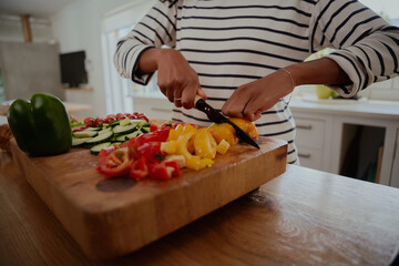Closeup of woman hands chopping yellow and red bell peppers on wooden chopping board in modern kitchen