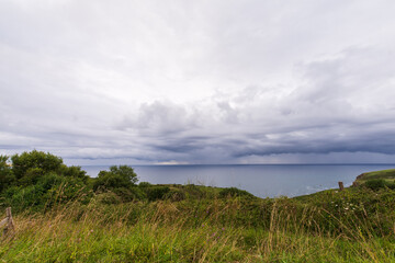 Fototapeta na wymiar View of cloudy blue sky, green field and sea in the background, horizontal