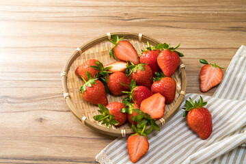 Tasty red fresh organic strawberries inside a bamboo plate with napkin on wooden background.