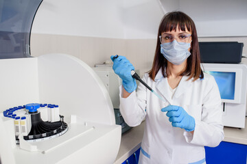 Young woman doctor laboratory assistant is using a micropipette test tubes near a fully-automated...