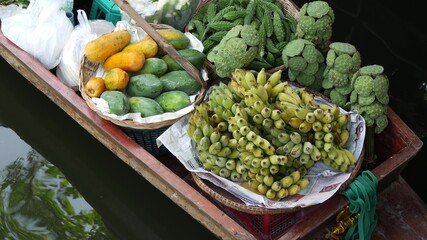 Iconic asian Lat Mayom floating market. Khlong river canal, long-tail boat with tropical exotic colorful fruits, organic locally grown vegetables. Top view of harvest and street food in wooden canoe