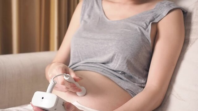 asian woman using pocket fetal doppler to monitor baby heart beat. expectant mother happy and smile when examine belly.