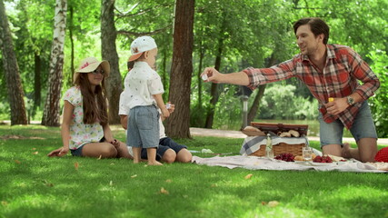 Positive parents blowing soap bubbles with children in park