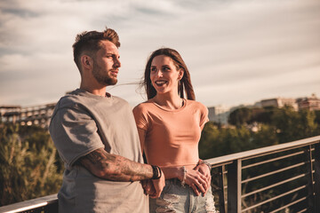 Young engaged couple posing serious and amused along the railing of an urban environment