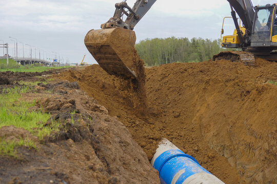 From the large bucket of a crawler excavator, the earth pours out into the trench where the pipe is laid.