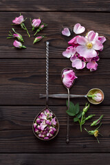 Rosehip fresh and dried flowers on a dark wooden table. Composition with rose hip flowers and metal spoons in the sun. Preparation of tea, tincture or essence. Cosmetology, culinary, medicine. © KashtykiNata