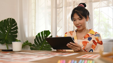 Ux Ui developer is working with a computer tablet while sitting at the wooden working desk.