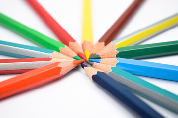 Fototapeta premium Many different colored wood pencil crayons placed on a white paper in a circle