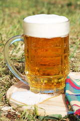 glass mug with beer and foam on a wooden tray on the grass
