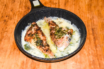 two fried perches in a cast iron pan in white sauce lie on a wood