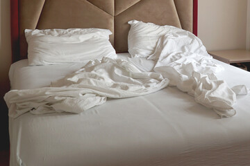     An unmade bed with white linens and wrinkled sheets.