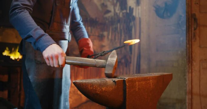 Caucasian blacksmith working in antique forge and forging while beating with hammers on metal item. Producing of iron things. Smithy manufactory concept. Man smithing and making steel thing.