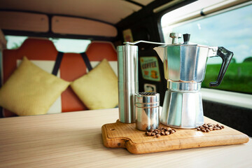 Aqua Bialetti stovetop coffee maker, coffee grinder, chocolate shaker and coffee beans, about to prepare coffee on a wooden tray in a cosy camper van