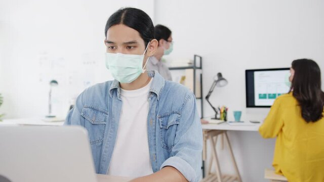 Asia businessman entrepreneur wearing medical face mask for social distancing in new normal situation for virus prevention while using laptop back at work in office. Lifestyle after corona virus.