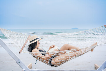 A woman is lying in a hammock and reading a book At a beach On her vacation.