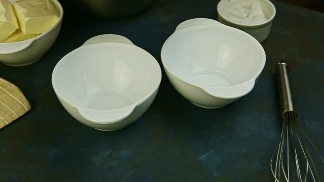 slow motion closeup woman hands ready to brake raw eggs into empty white bowls