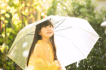 Asian girl is wearing yellow raincoat and enjoying rainfall in the park. Kid playing on the nature outdoors.