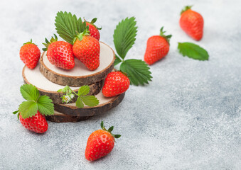 Fresh raw organic summer strawberries with a lot of vitamins and leaf on round timber boards on light background.