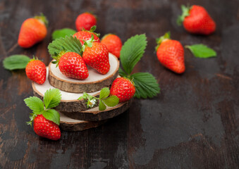 Organic fresh raw strawberries with leaf on timber round boards on dark background.