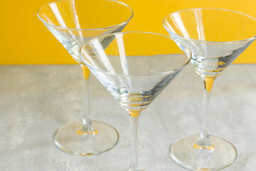 Three empty transparent martini glasses on a yellow background. Cocktail container
