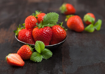 Fresh raw organic strawberries with leaf in steel bowl on wooden background.