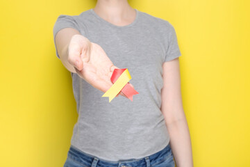 World Hepatitis Day concept. Girl in gray T-shirt holds in her hand awareness symbol red-yellow ribbon. Yellow background