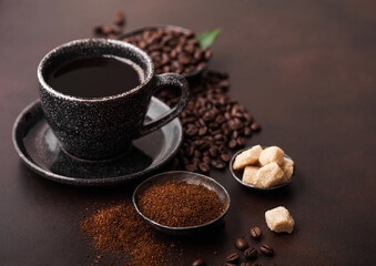 Cup of fresh raw organic coffee with beans and ground powder with cane sugar cubes with coffee tree leaf on brown background.