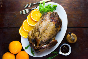 Festive roast duck on wooden table with oranges, hoi sin sauce and arugula leaves.