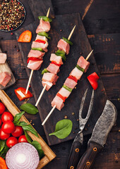 Raw pork kebab with paprika on chopping board with fresh vegetables on wooden background with fork and knife. Salt and pepper with lettuce and paprika and cherry tomatoes. Top view