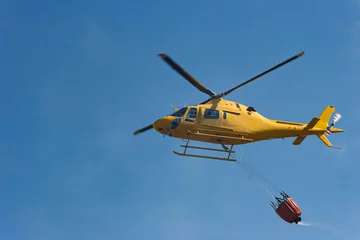 Poster Een brandweerhelikopter vervoert water om een brand te blussen die is ontstaan door de hitte van de zomer. © mestock