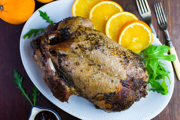 Festive roast duck on wooden table with oranges, hoi sin sauce and arugula leaves.