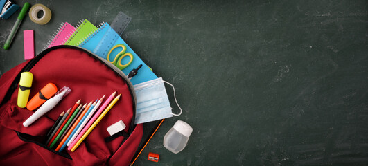Backpack full of school supplies and mask on blackboard top