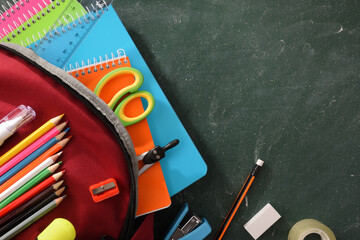 Fototapeta na wymiar Backpack full of school supplies on green blackboard detail top