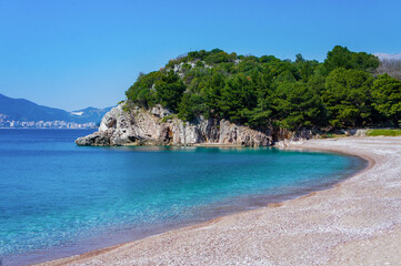 Fototapeta premium Mediterranean blue sea, beach with small orange pebbles, rocks with green pine trees.
