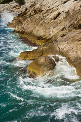 Waves of the blue sea break foaming at warm colored rocks.