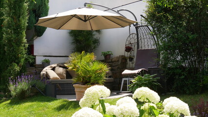 Loungegruppe und Hängesessel mit Sonnenschirm in einer Gartenecke umgeben von einer Palme und...