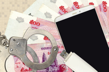 500 Cambodian riels bills and smartphone with police handcuffs. Concept of hackers phishing...