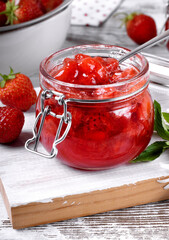 Strawberry jam in glass jar on the white wooden table