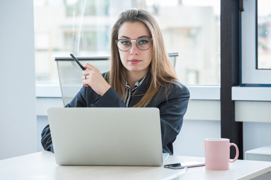 giovane manager bionda con occhiali da vista è seduta nella sua poltrona di lavoro davanti alla scrivania con il portatile e guarda con aria seria
