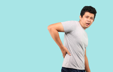 Asian man suffering from backache,Lower back pain on light blue background in studio With copy space. 