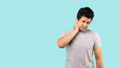 unhappy Asian man suffering from neck pain on light blue background in studio With copy space.