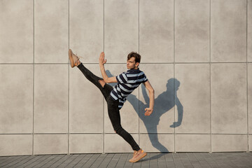 Fototapeta na wymiar Jumping young buinessman in front of city building wall, on the run in jump high. Hurrying up, moving to daily routine inspired and sportive. Young ballet dancer in casual clothes and sunshine.