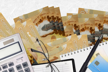 100 Canadian dollars bills and calculator with glasses and pen. Tax payment concept or investment...